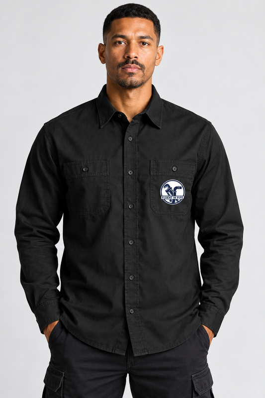A man wearing a black long-sleeve button-up shirt with a circular blue and white logo patch on the left chest pocket, posed against a light gray studio background.